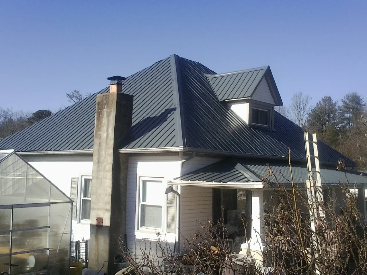 Dark blue standing seam metal roof on a white farmhouse with dormer — Slate & Tile Roof Repair by Roofing Brothers in Highfalls