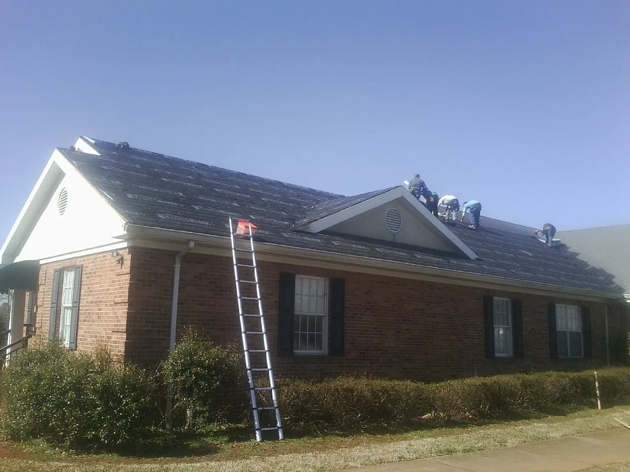 Crew tearing shingles off a brick ranch roof with a ladder set — Metal Roof Repair work by our crew in Highfalls