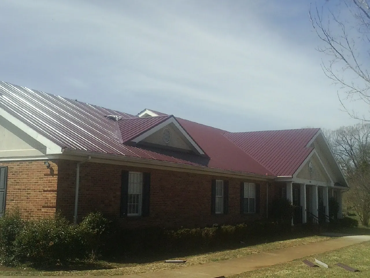 Red metal roof with gabled entries on a long brick building, from a Hail Damage Roof Repair job in Highfalls