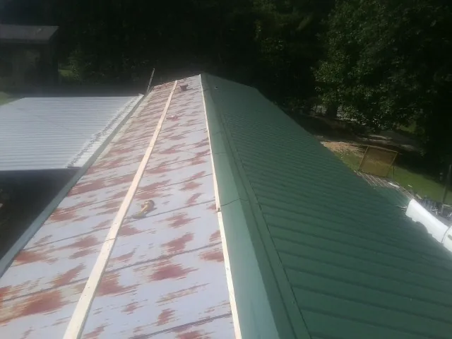 Old rusted panels beside newly installed green metal roofing — Wind Damage Roof Repair by Roofing Brothers in Highfalls