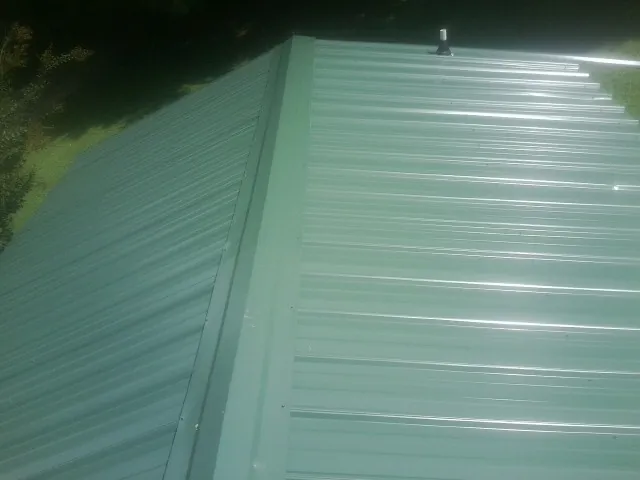 New green metal panels meeting at the ridge of a roof — Flat Roof Repair work by our crew in Highfalls