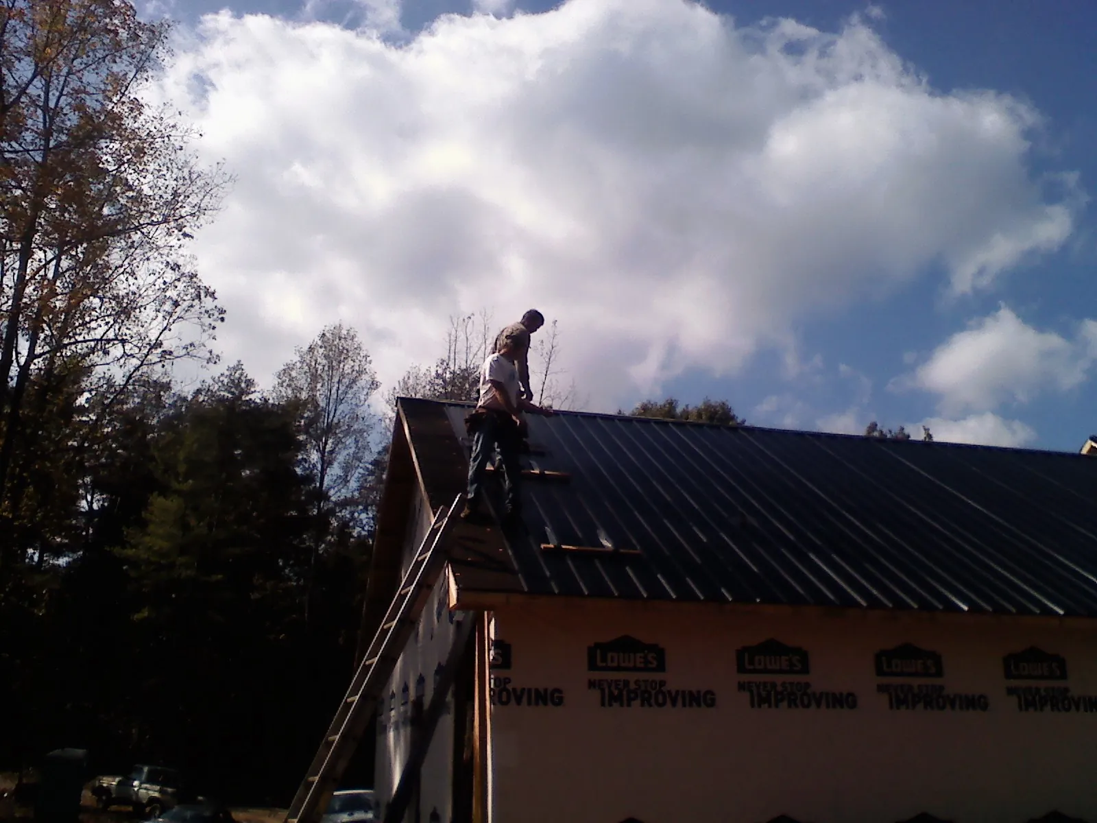 Roofer fastening dark metal panels high against a cloudy sky, from a Roof Inspection job in Highfalls