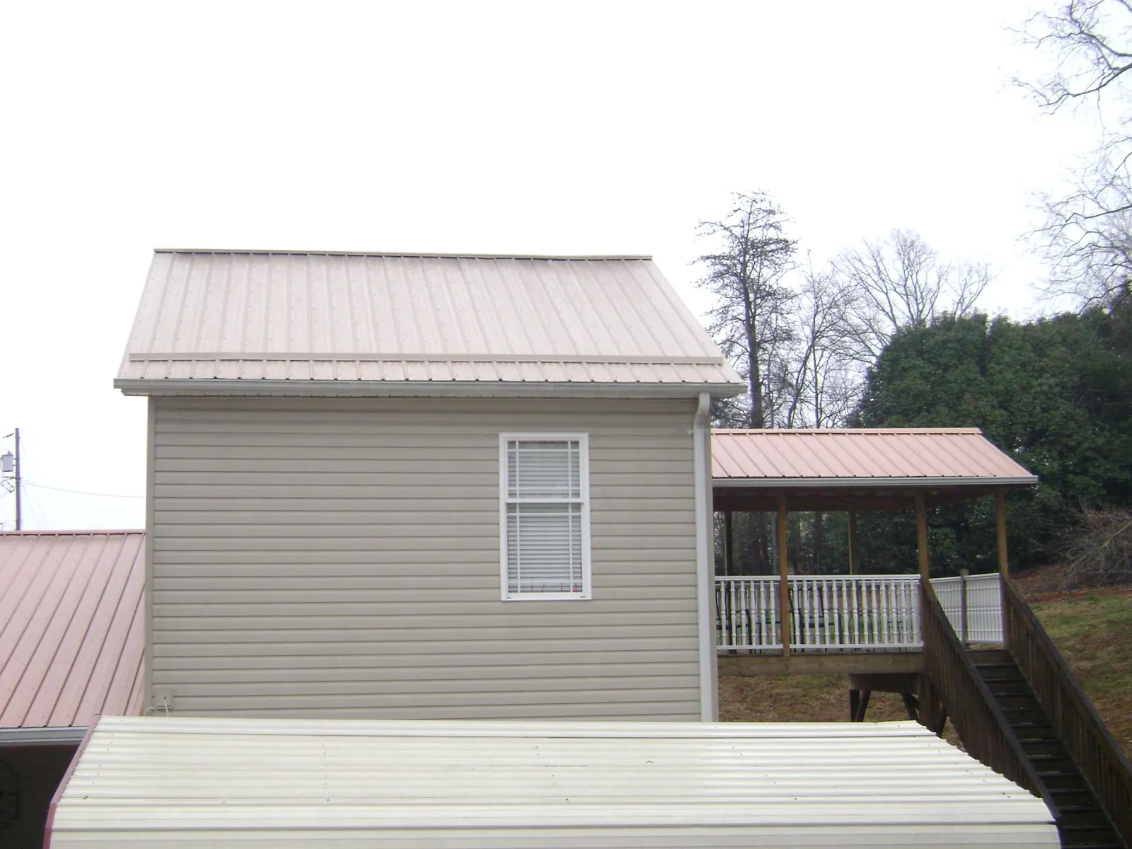 Tan metal roofs on a two story addition and attached porch, from a Roof Replacement job in Highfalls